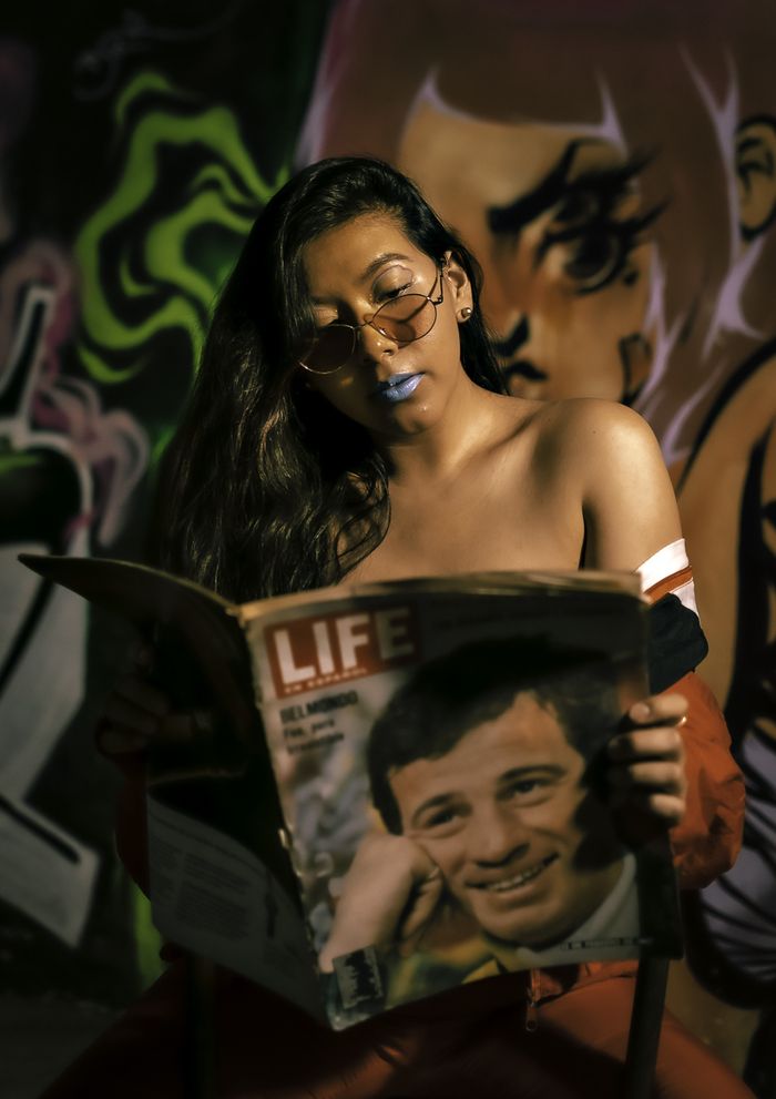Woman in sunglasses reads a magazine against vibrant graffiti backdrop in Mexico City.