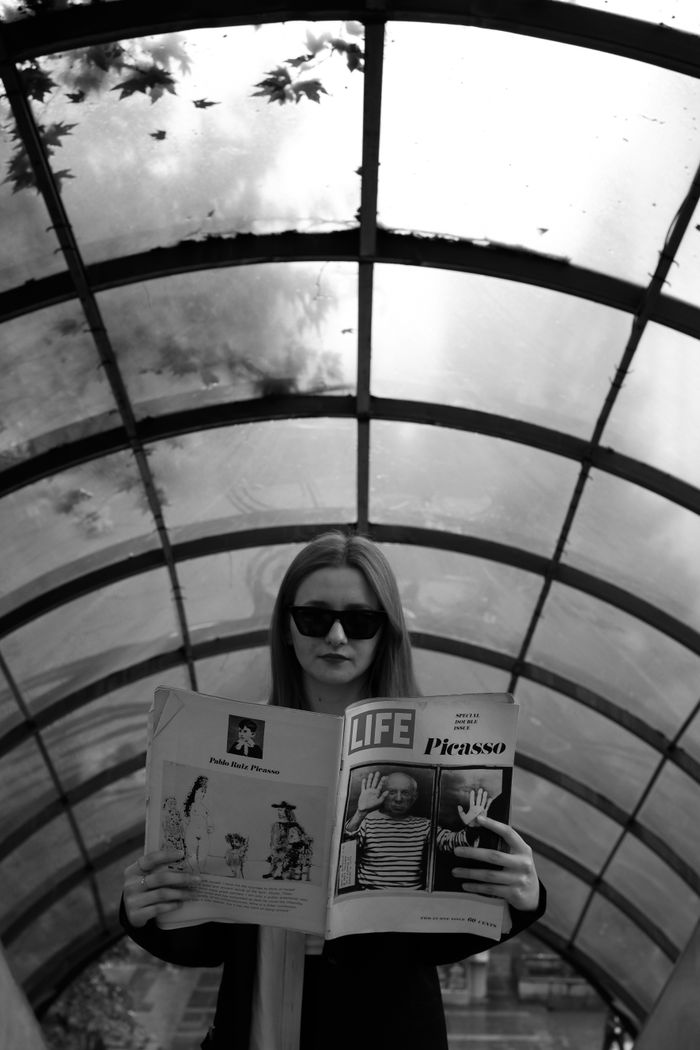 A stylish woman in sunglasses enjoys a Life magazine under a glass canopy, exploring urban lifestyle and art.