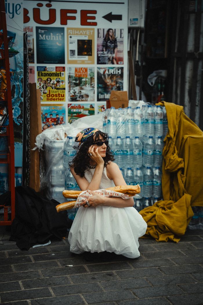 Crafting Captivating Headlines: Your awesome post title goes here Woman in a white dress sitting by a magazine stand, holding baguettes and wearing a headscarf.